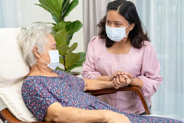 Caregiver with face mask help and support Asian senior woman with love and care in home and prevention of disease