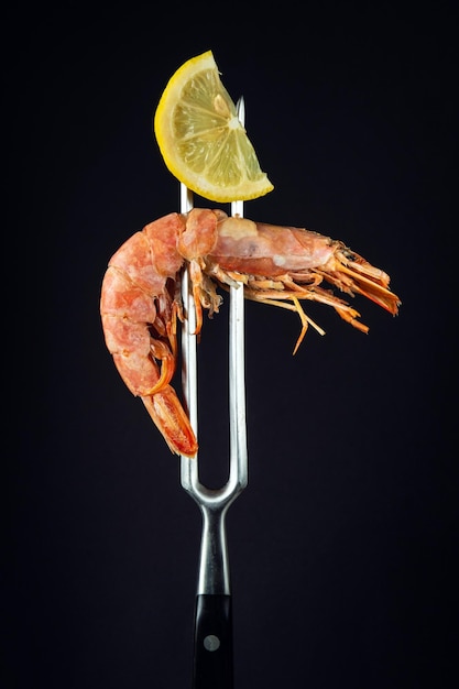 Caridea or prawn with a slice of lemon on a fork Idea of delicious street or restaurant food on black background with space for menu or recipe