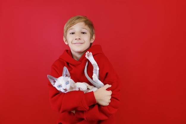 A caring boy in a red suit holds a white kitten in his arms presses him to himself and hugs