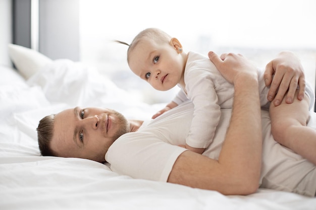 Caring father holding little baby on belly in bed