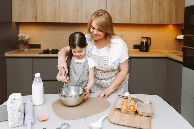 Caring grandmother and little granddaughter are having fun baking cookies together in the home kitchen A loving elderly grandmother and granddaughter prepare a delicious sweet cake