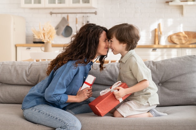 Caring mom and son sit bonding on couch hold gift mother and adorable small kid exchanging presents