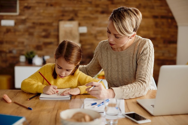 Caring mother assisting her daughter in drawing at home