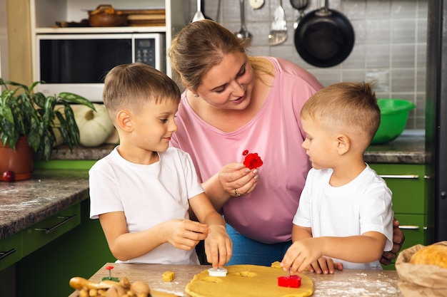 Caring mother help little preschooler sons prepare cookies, smiling loving mom learn cooking with small boys child, making lunch on weekend in kitchen together