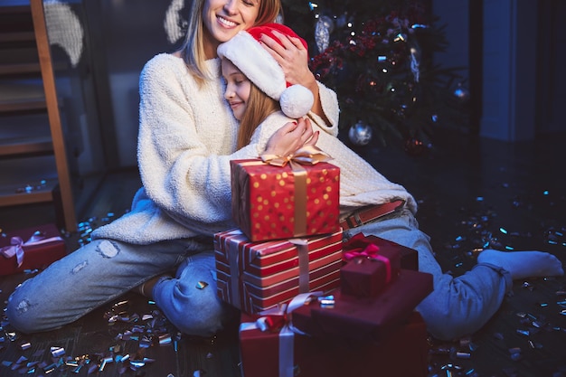 Caring mother hugging daughter near New Year tree