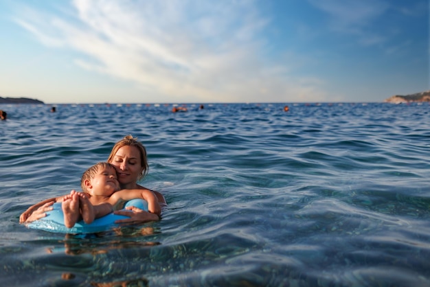 Caring mother rides her son on an inflatable ring in the sea