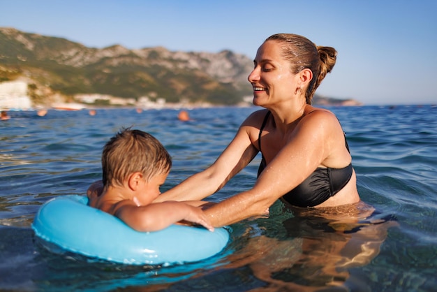 Caring mother rides her son on an inflatable ring in the sea