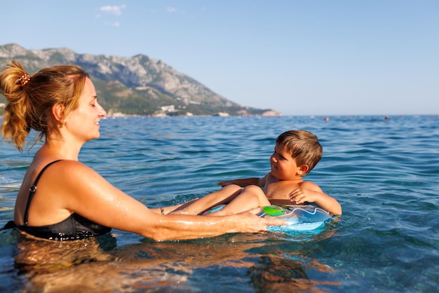 Caring mother rides her son on an inflatable ring in the sea