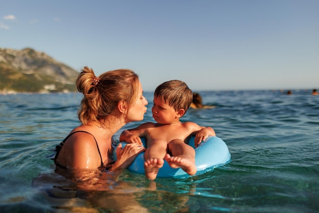 Caring mother rides her son on an inflatable ring in the sea