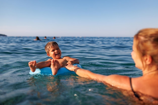 Caring mother rides her son on an inflatable ring in the sea