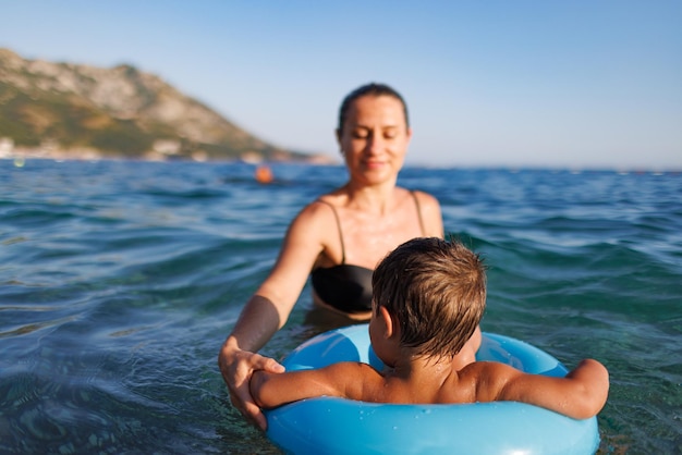 Caring mother rides her son on an inflatable ring in the sea