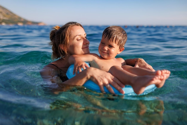 Caring mother rides her son on an inflatable ring in the sea