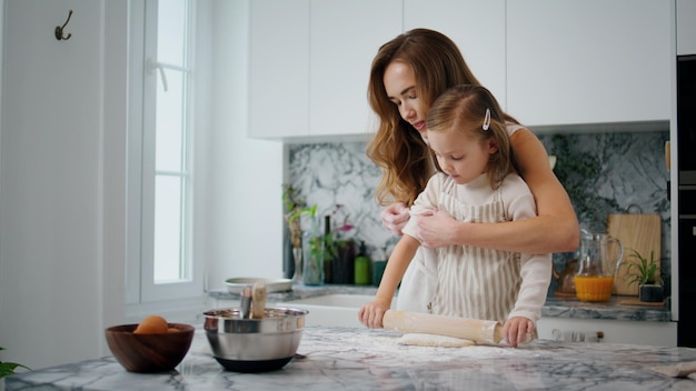 Caring mother rolling sleeves to daughter at kitchen closeup Kid helping parent