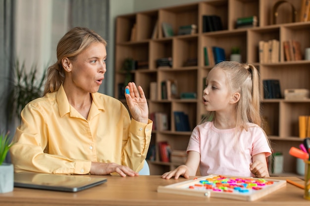 Photo caring mother teaching small preschool child daughter pronouncing words and letters correctly