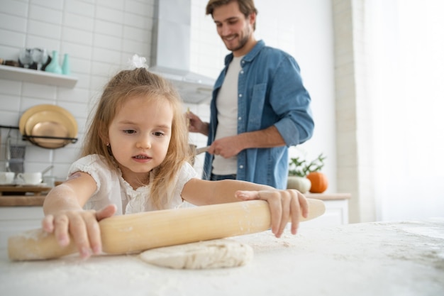 Caring young Caucasian father and cute little preschooler daughter bake in kitchen at home together, happy loving dad teach small girl child cooking, preparing pancakes or biscuits for breakfast