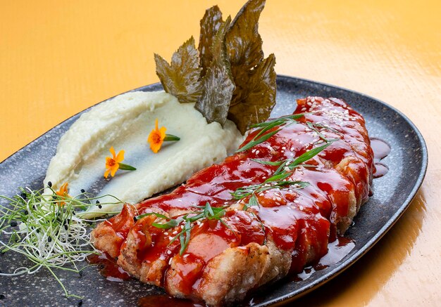 Carp in sweet and sour Chinese sauce with mashed potatoes and grape leaves On a dark ceramic platter