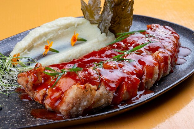 Carp in sweet and sour Chinese sauce with mashed potatoes and grape leaves On a dark ceramic platter