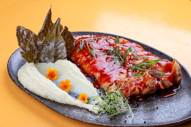 Carp in sweet and sour Chinese sauce with mashed potatoes and grape leaves On a dark ceramic platter