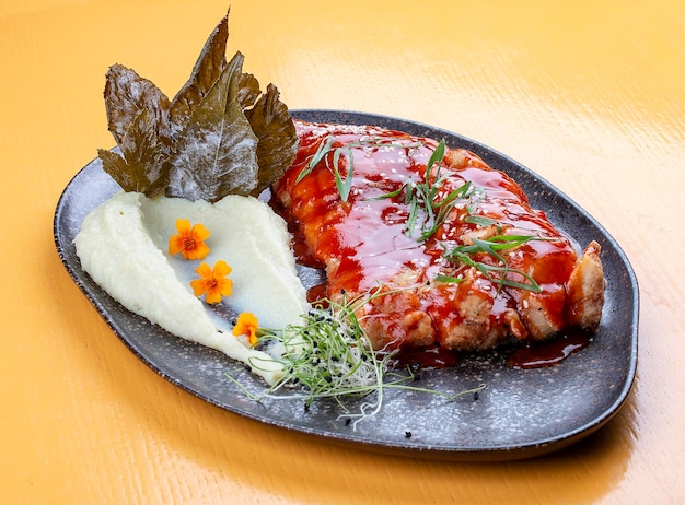 Carp in sweet and sour Chinese sauce with mashed potatoes and grape leaves On a dark ceramic platter