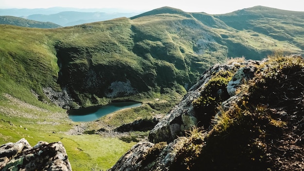 Carpathian lake Brebeneskul and rocky terrain against background of green mountains