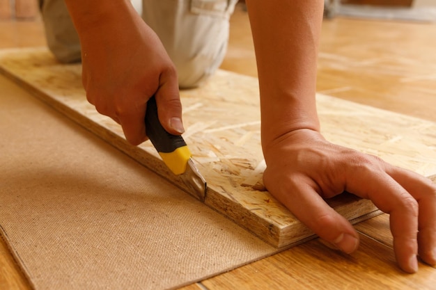 Carpenter cuts fiberboard with a mounting knife using OSB