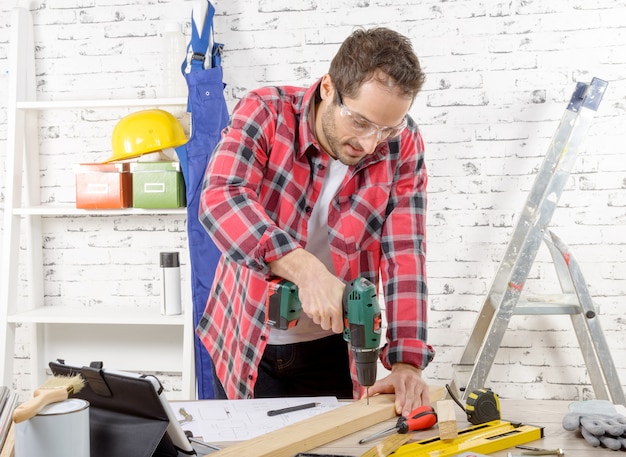 Photo carpenter drilling hole in plank in his workshop