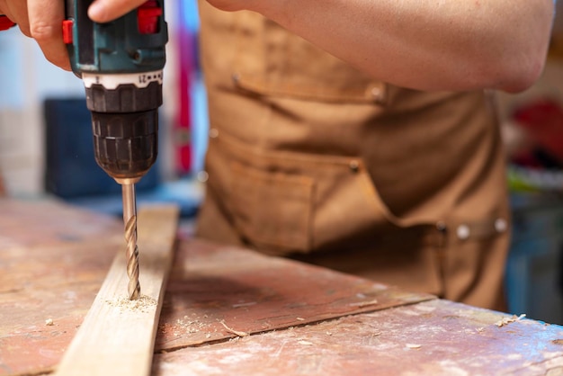 Carpenter drills a hole in wooden plank with an electrical drill