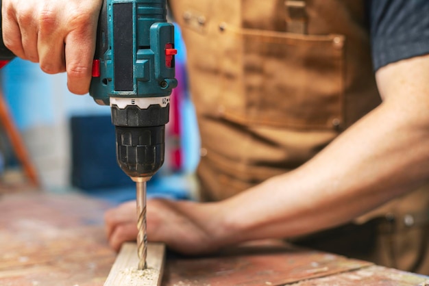 Photo carpenter drills a hole in wooden plank with an electrical drill