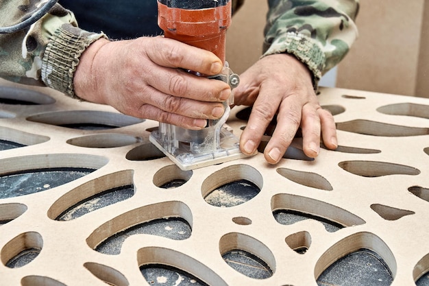 Carpenter milling holes in MDF decorative partition wall with a hand electric router machine