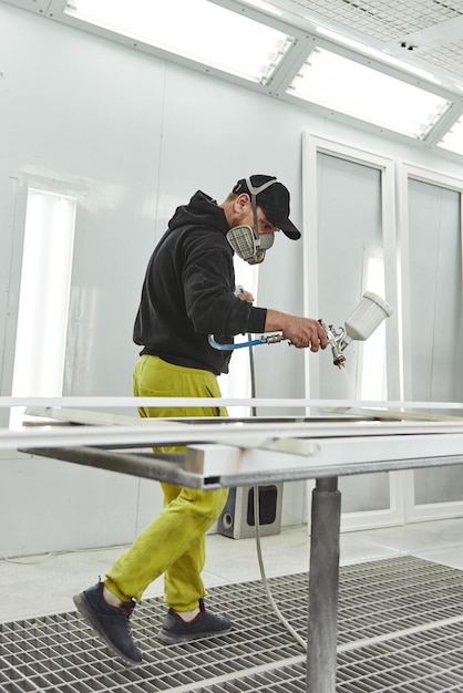 The carpenter paints furniture details in white color in the carpentry shop Vertical shot Side view