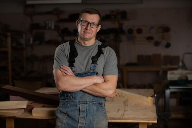 A carpenter stands with his arms crossed in his woodworking shop