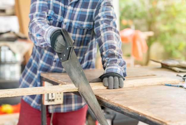 Photo a carpenter ware gloves use hand saw to sawing wood