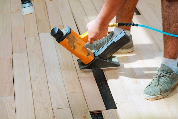 Photo carpenter worker installing wood parquet board during flooring work with hammer