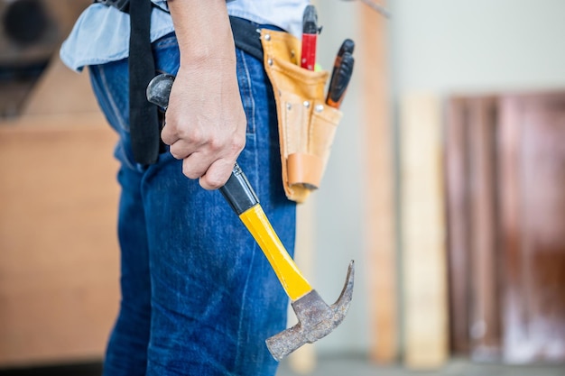 Carpenter working in wood workshop Handyman manual worker in tools belt and holding hammer in his hands