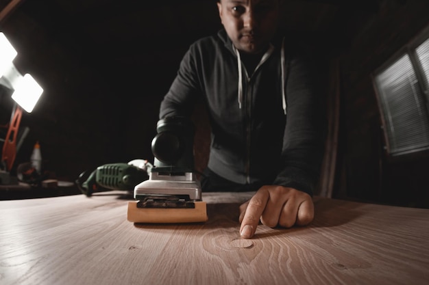 A carpenter works in a workshop Joiner's grinders furniture manufacturing A carpenter is grinding a wooden part with an electric sander