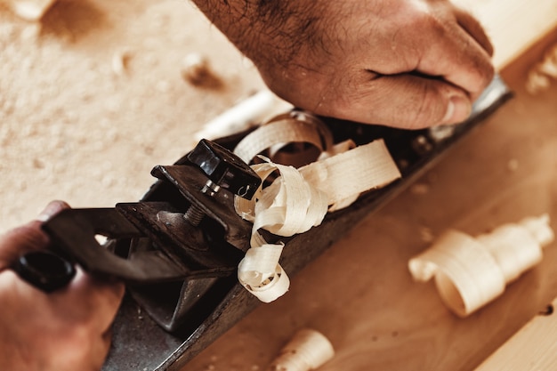 Carpenters hands planing a plank of wood with a hand plane