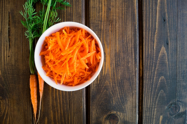 Carrot grated in a bowl, on a wooden table.