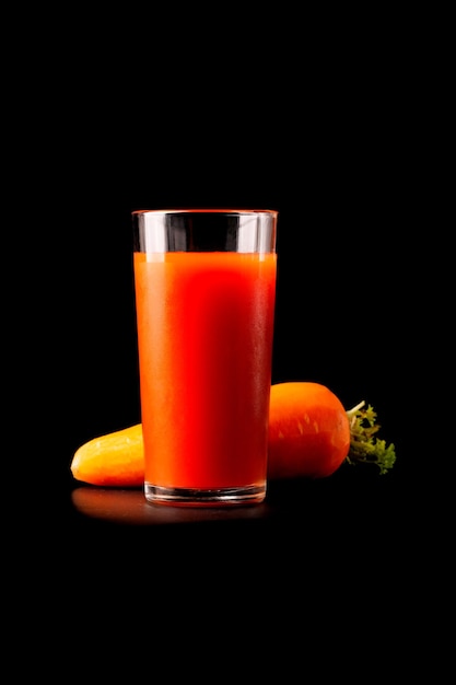 Carrot juice in a tall glass glass with natural fresh tomatoes on a black background