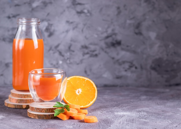 Carrot and orange juice in bottle and glass on wooden stands