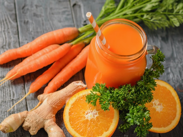 Carrot smoothie, two orange halves, ginger root and parsley on a wooden table.