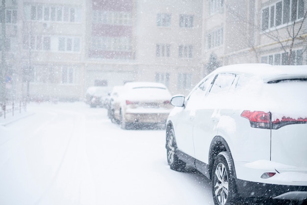 Cars covered under snow during winter, stormy weather outside