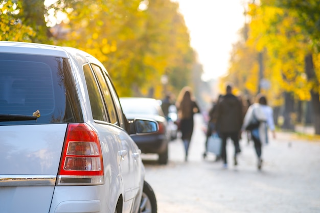 Cars parked in a row on a city street side on bright autumn day.