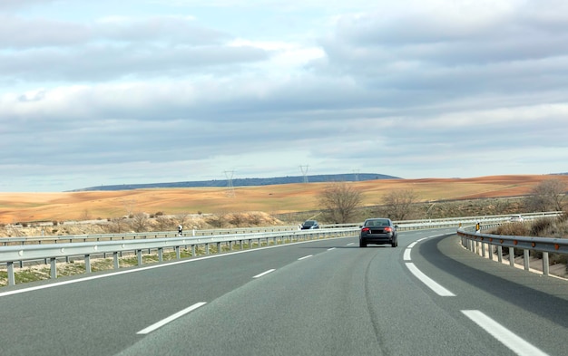 Cars traveling on the highway between brown hills with a cloudy sky