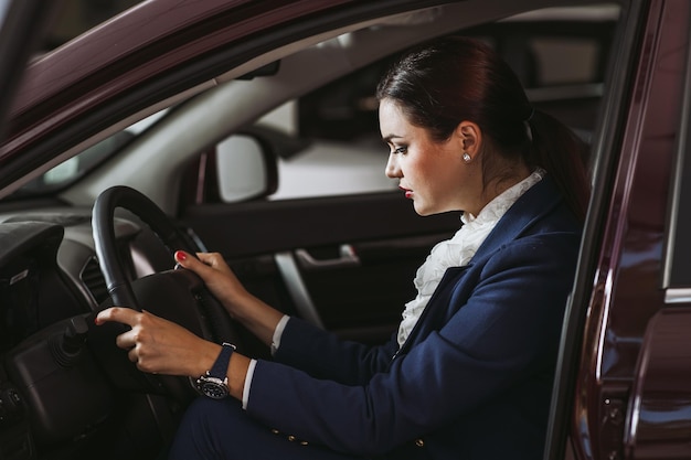 CarSatisfied happyEuropean female client customer woman sitting at the wheel of new car