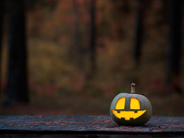 Carved glowing pumpkin on a wooden table in the autumn forest for Halloween Copy space