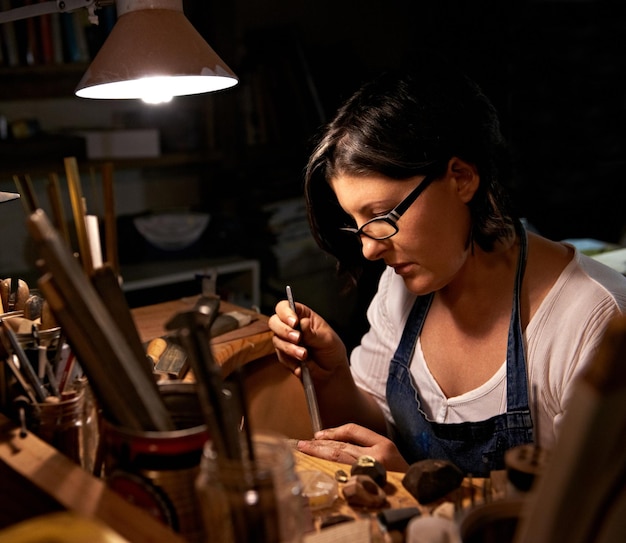 Carving wood and artist in workshop with creative project or unique sculpture on table at night Artisan carpenter and woman with talent for creativity in dark studio in process of woodworking