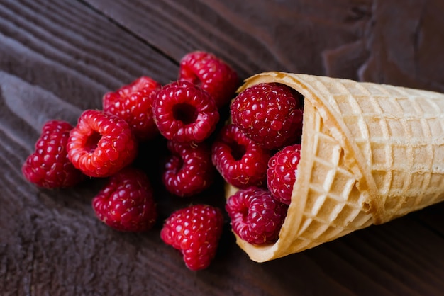 A cascade of fresh raspberries in a waffle cone of ice cream on brown. Close up