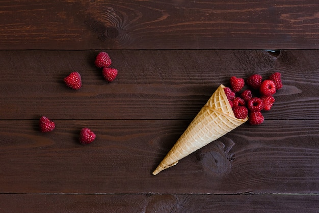  A cascade of fresh raspberries in a waffle cone of ice cream on brown. 