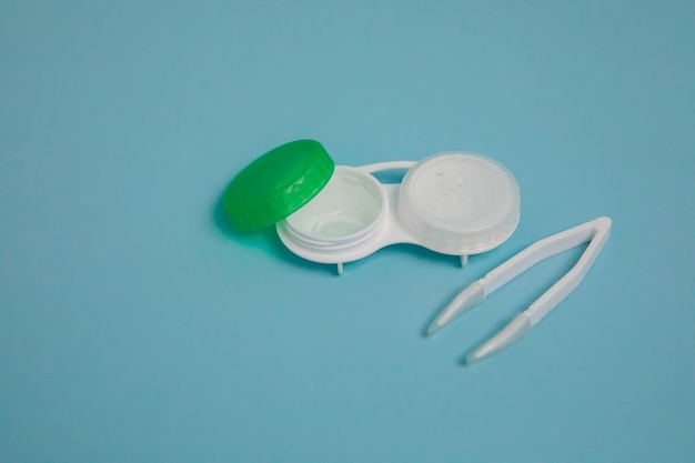 Case with contact lenses and tweezers on light blue background