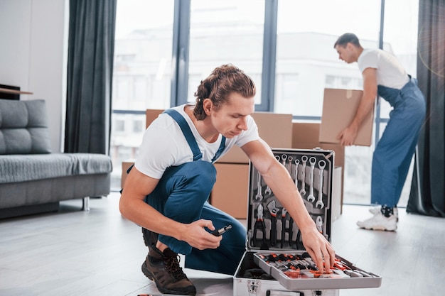 Case with equipment Two young movers in blue uniform working indoors in the room